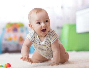 Ein Kleinkind krabbelt zuhause auf dem Boden und lacht.