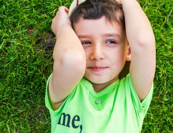 Fröhlich lächelnder kleiner Junge, der im Sommer auf dem Gras liegt.