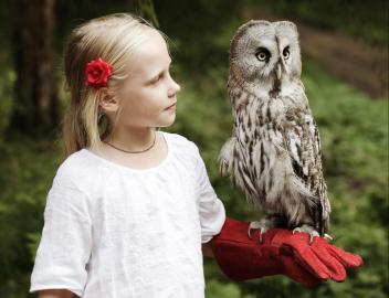 Ein blondes Mädchen mit einer Eule auf dem Arm.