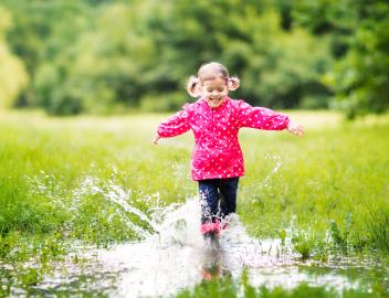 Ein Mädchen in linker Regenjacke springt in eine Pfütze